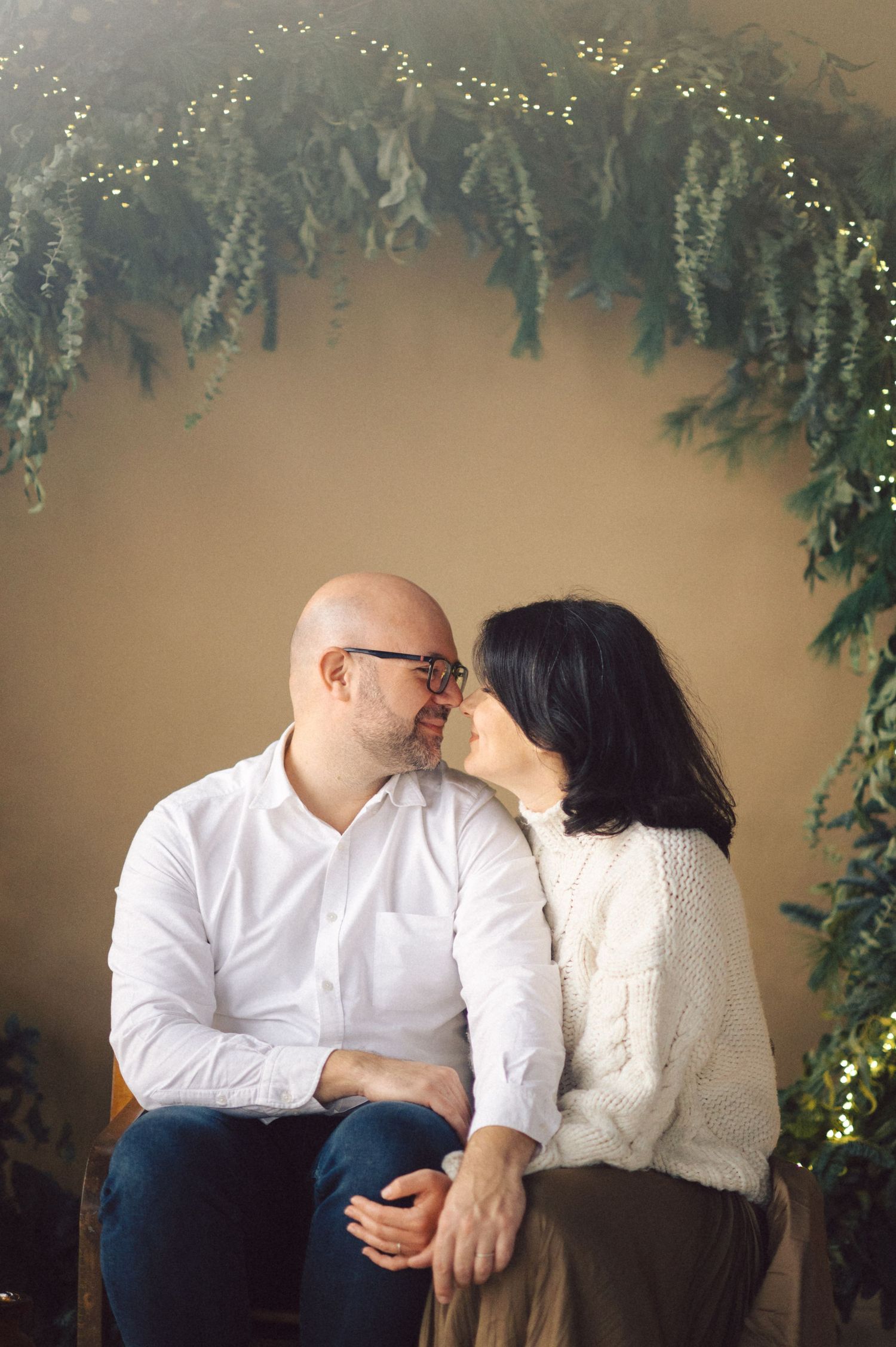 A romantic photoshoot series against a beige wall decorated with hanging greenery and twinkling lights.