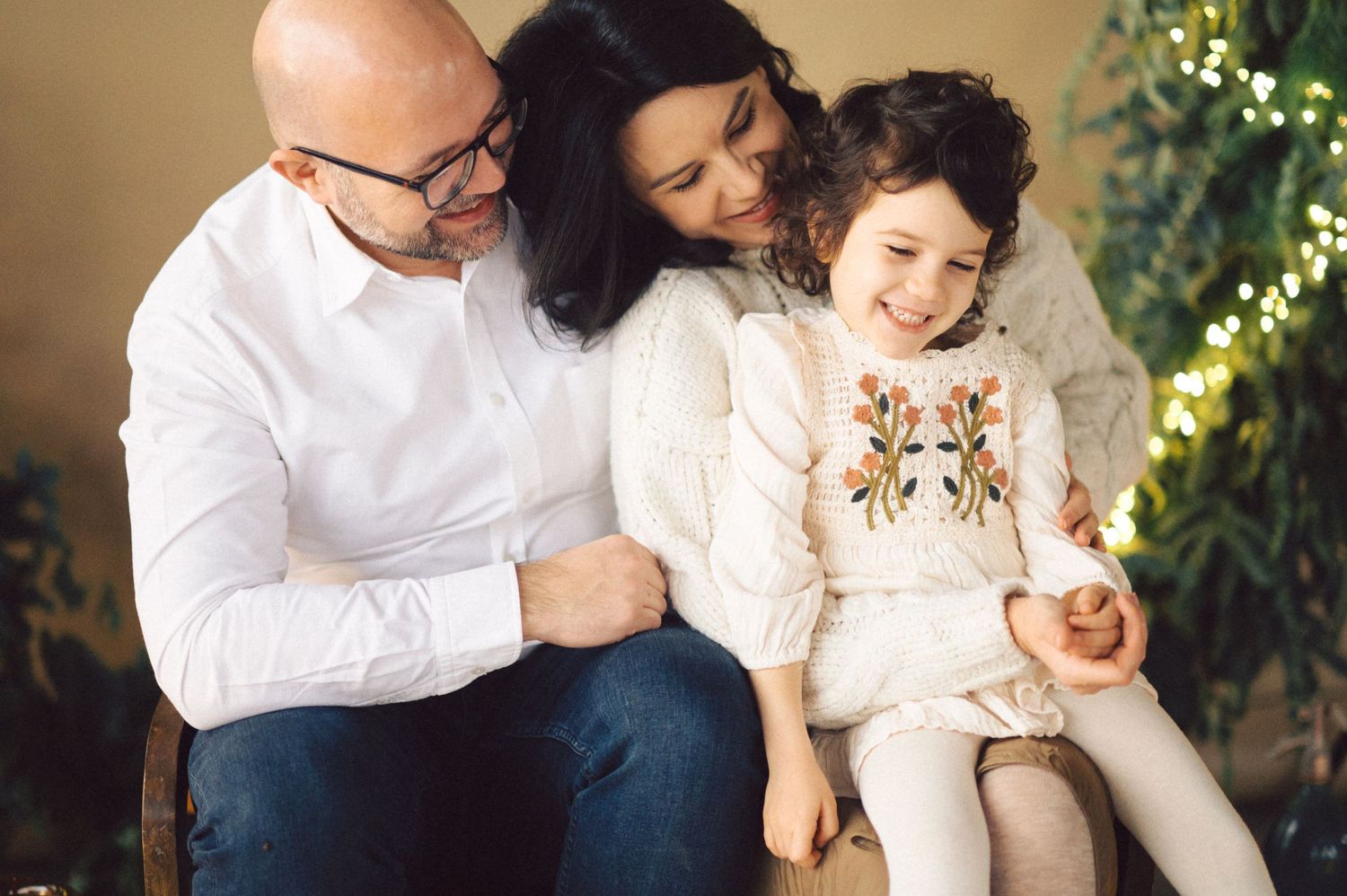 A family shares a joyful moment together while sitting by holiday decorations and twinkling lights.