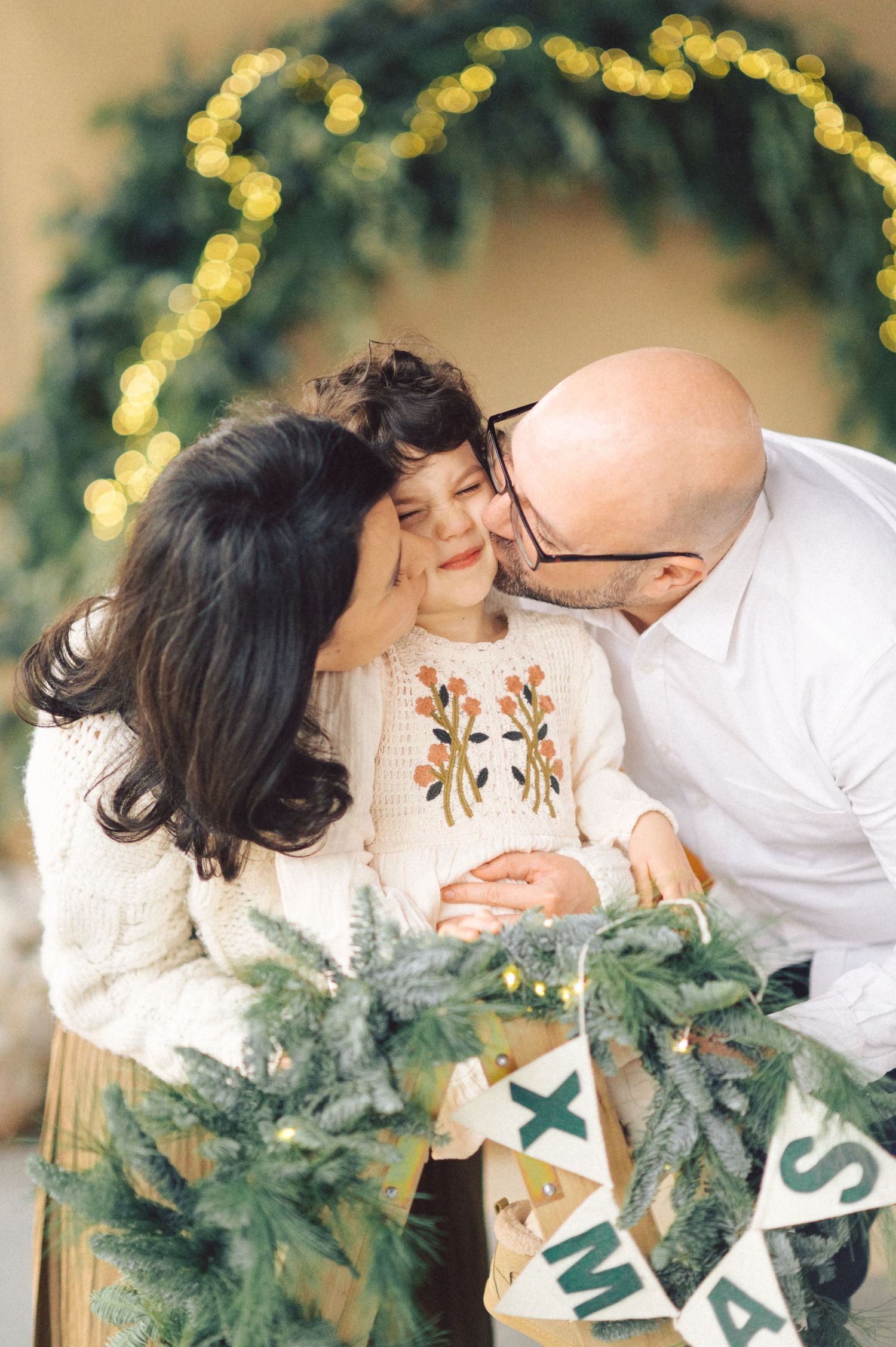 Family sharing an intimate holiday moment together with evergreen decorations and twinkling lights in the background.