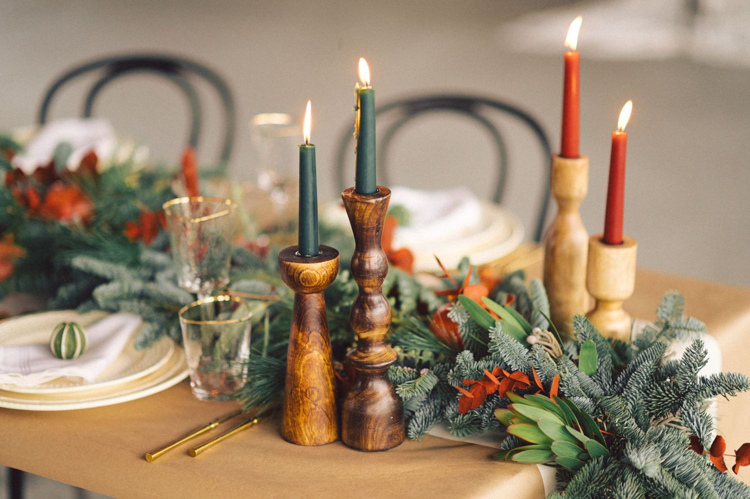 Decorative Christmas table setting with lit candles in wooden holders and evergreen garland with red berries.