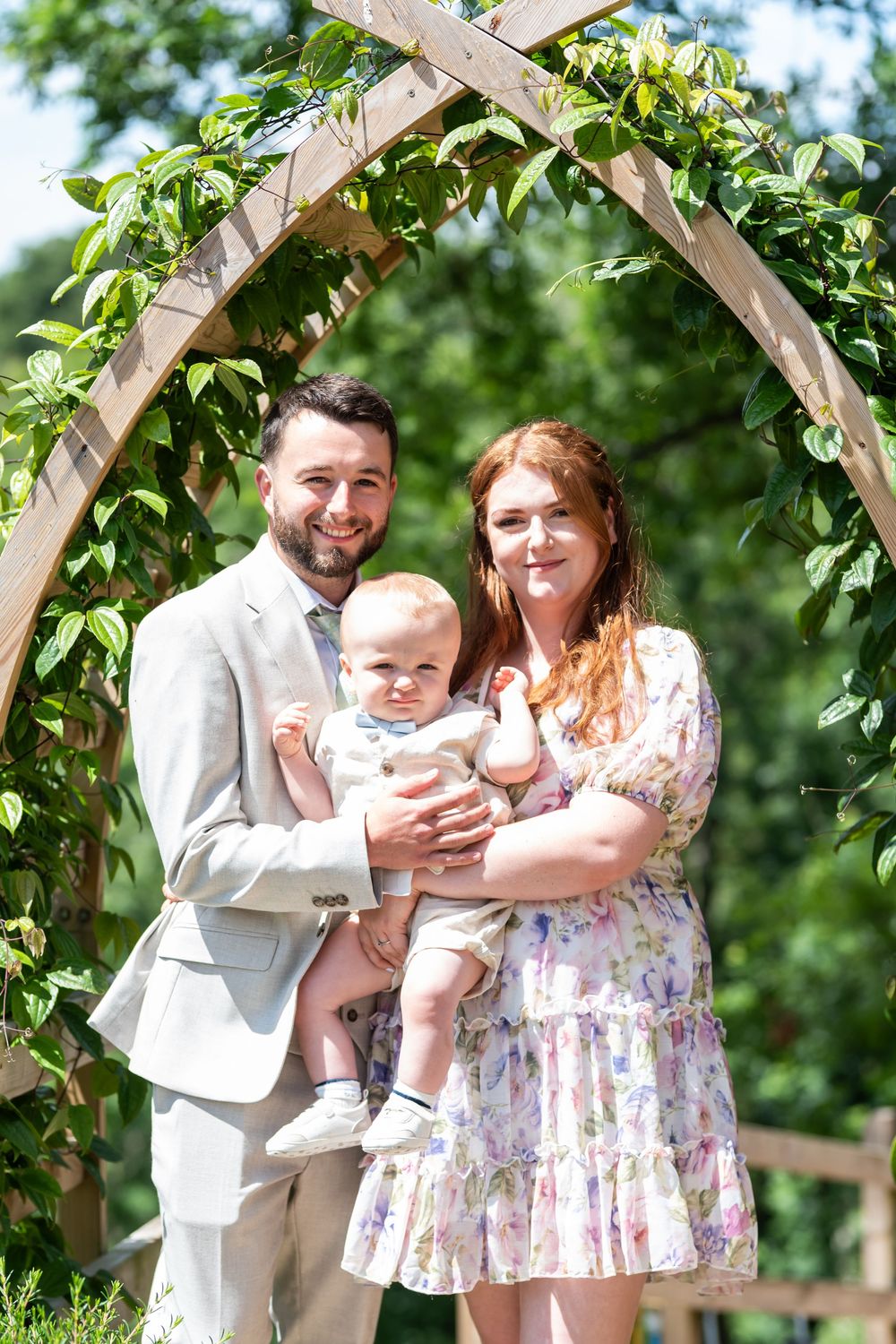 Family poses together under a vine-covered garden arch outdoors.