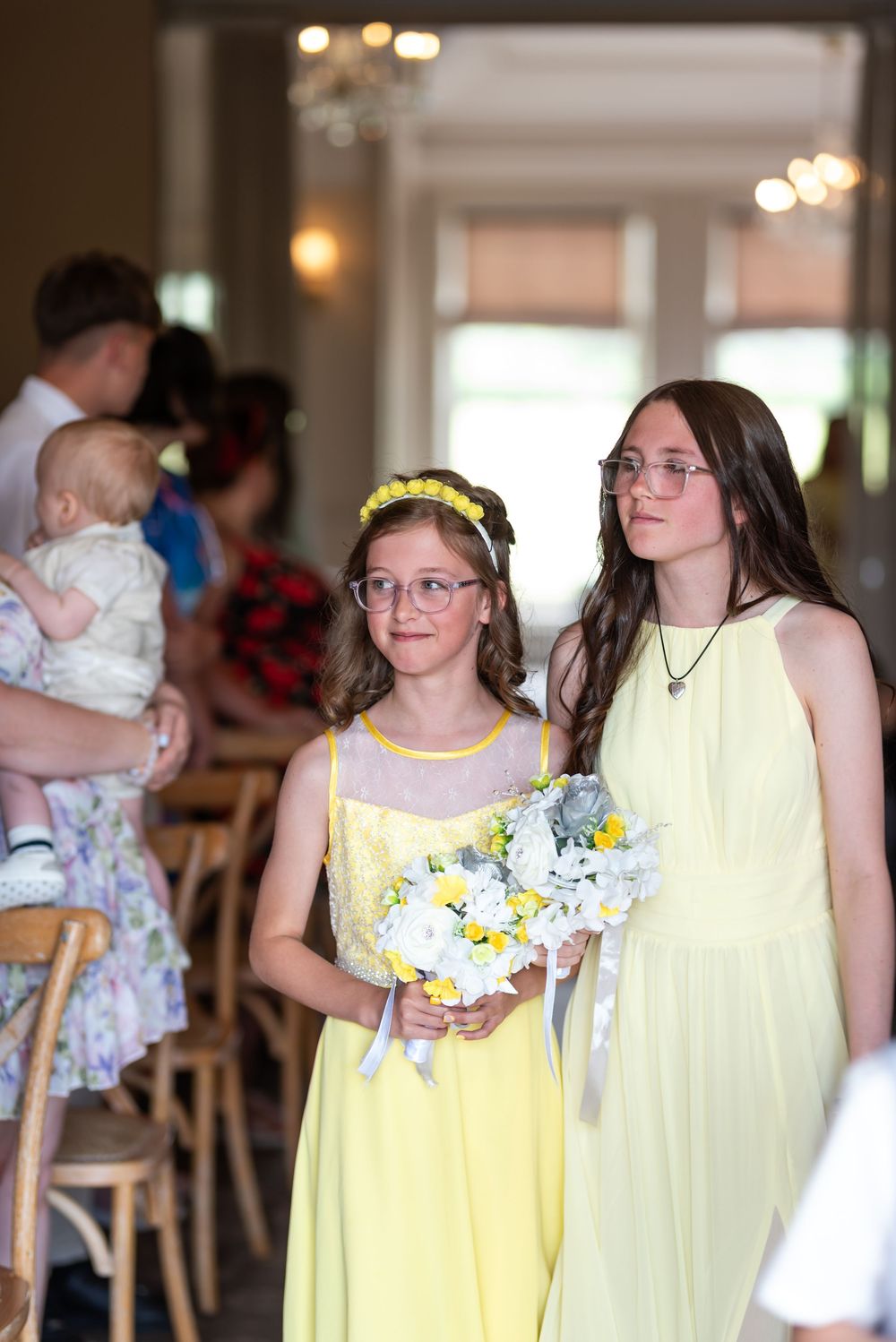 Bridesmaids wearing pastel yellow dresses lined up during wedding ceremony.