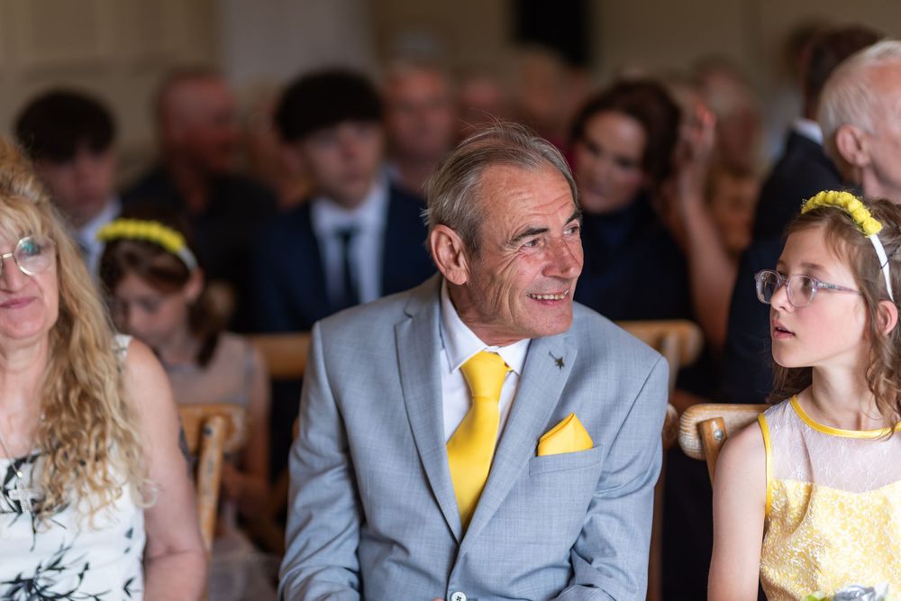 Wedding guests in formal attire with yellow accents seated at reception tables.