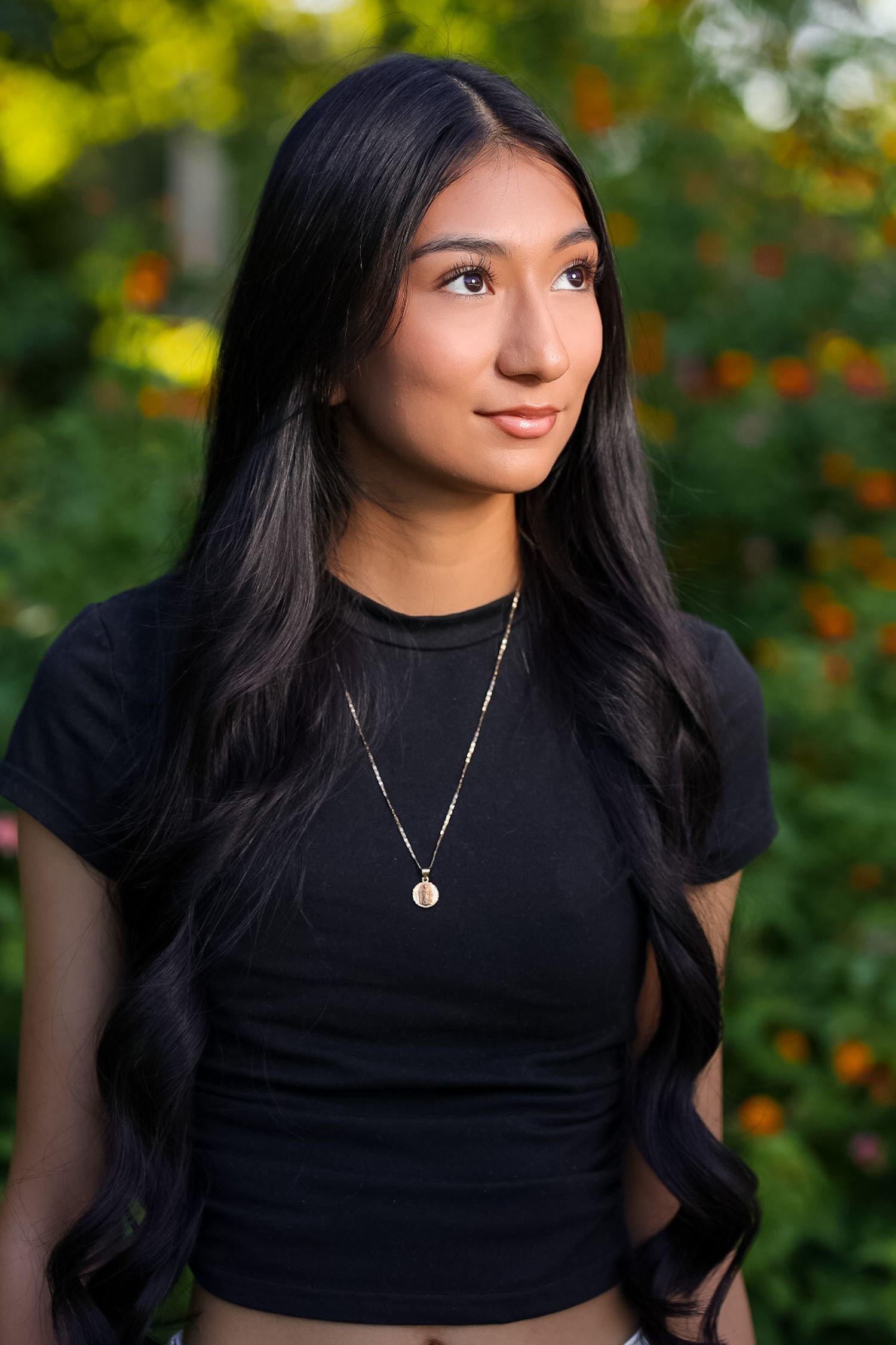 A portrait photo showing a person in a black top posing outside with greenery and orange flowers in background at Gulley Park