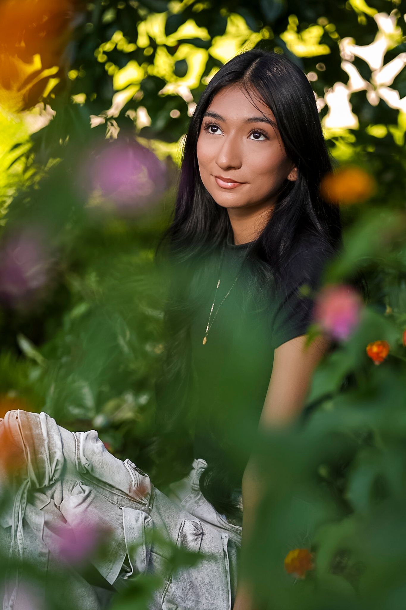 Woman in a white outfit poses elegantly among lush greenery and flowers in a dreamy outdoor garden setting at Gulley Park