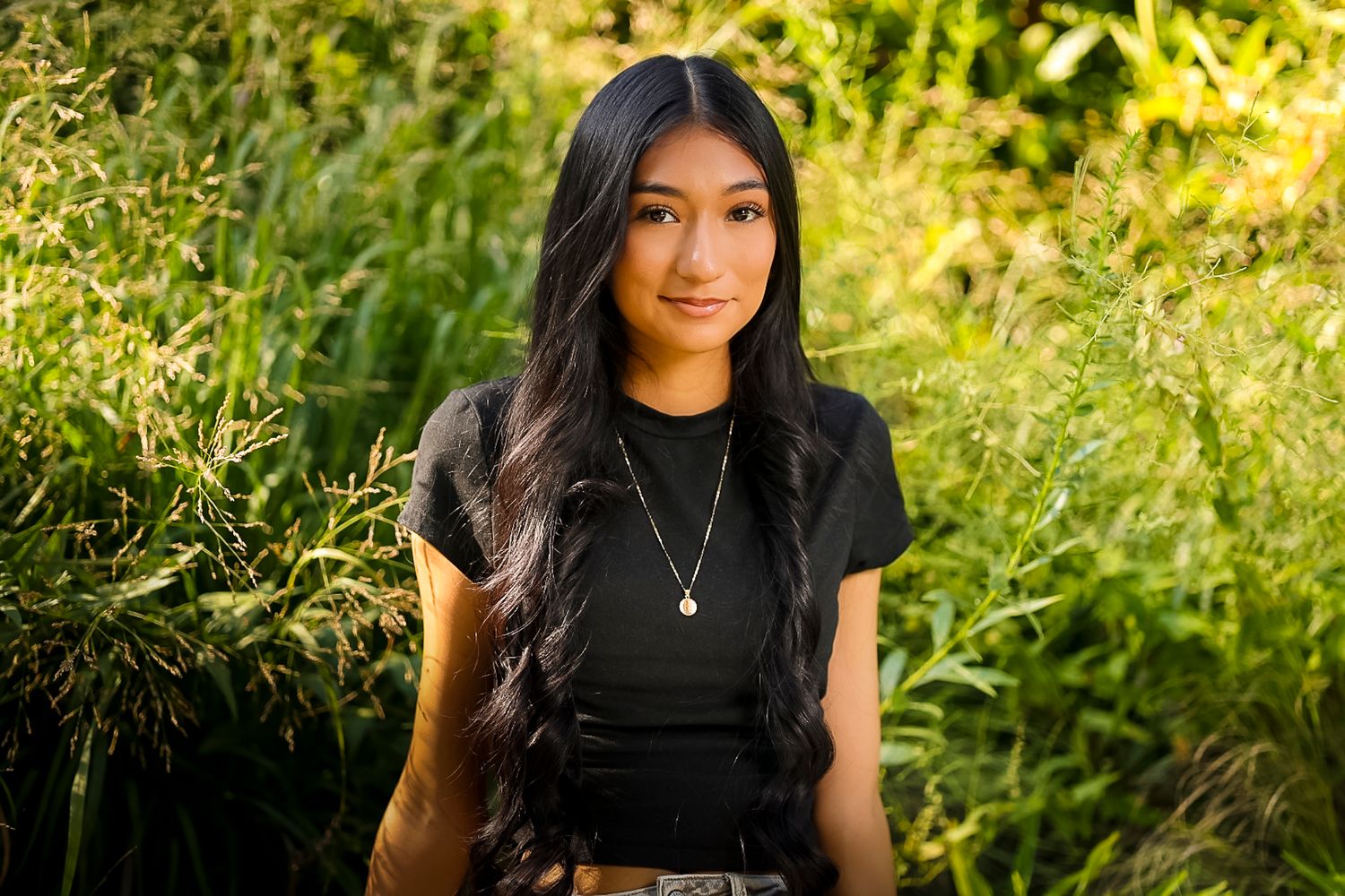 A person in a black top smiles while sitting in a sunlit garden with lush yellow and green foliage in the background at Gulley Park