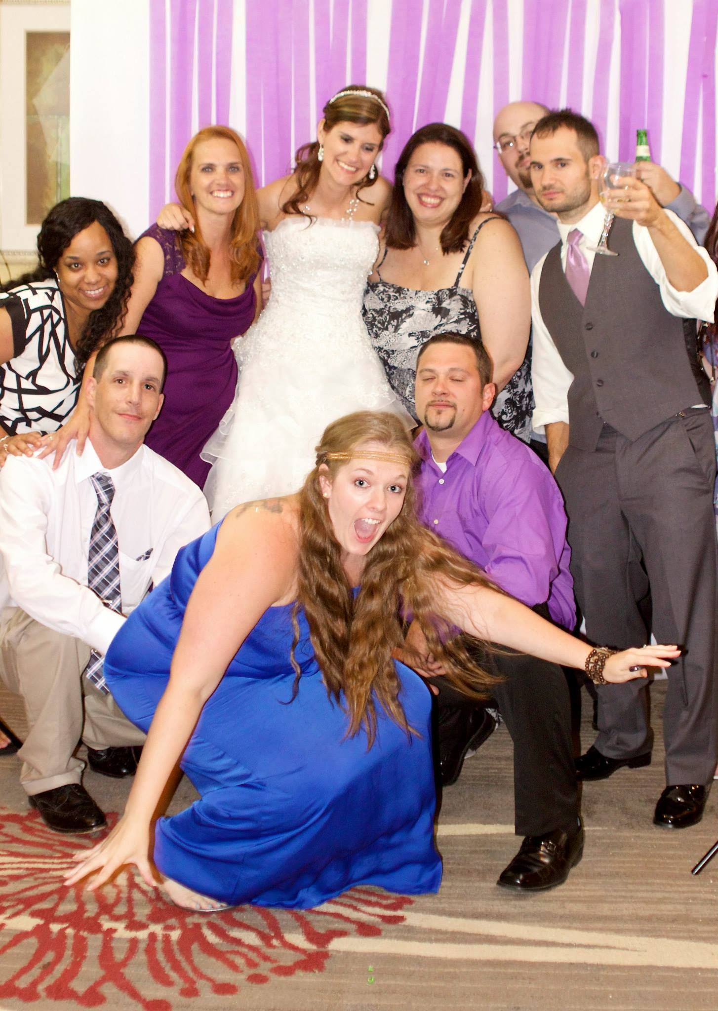 A group of wedding guests posing together at a reception with a bride in white and others in colorful attire.