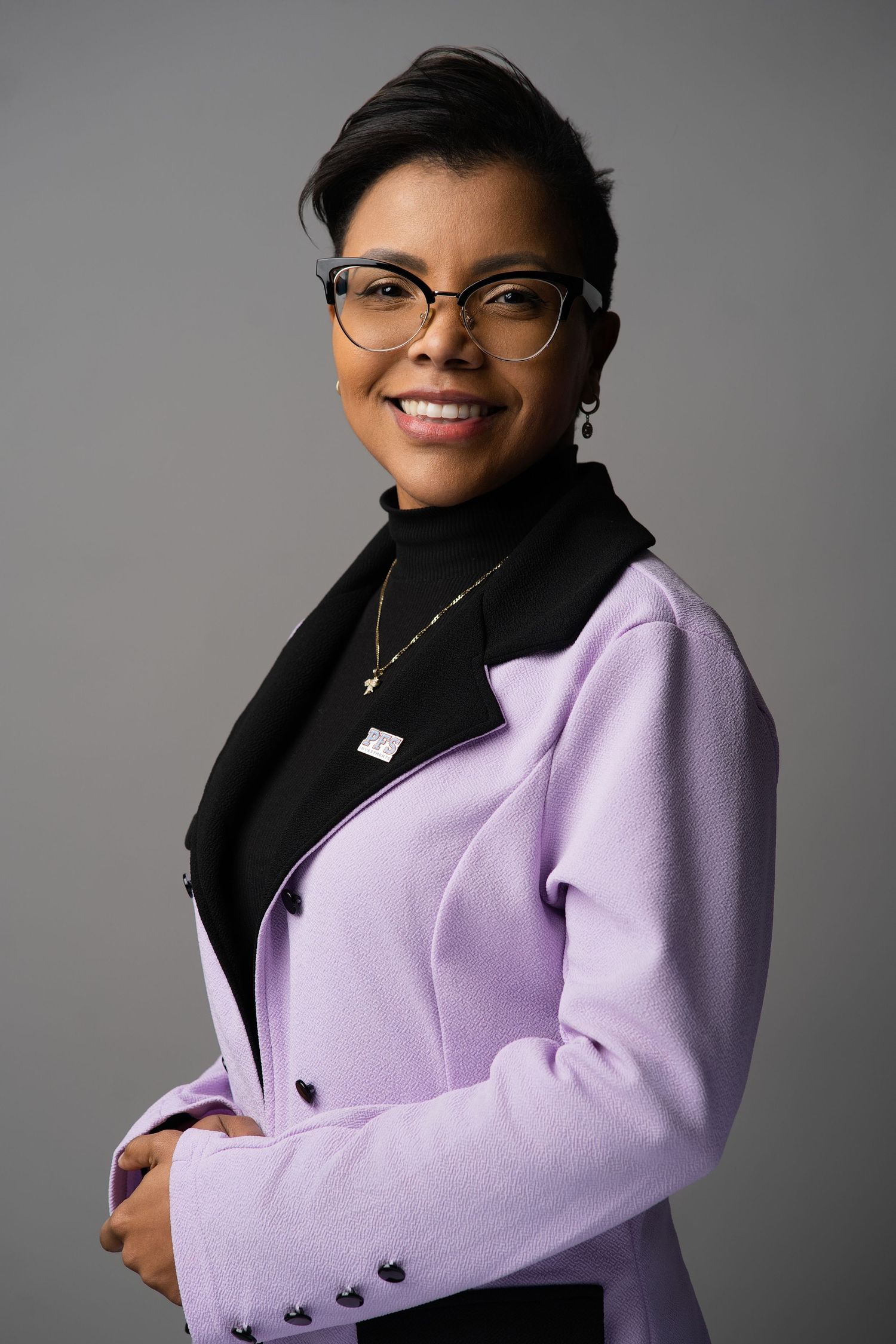 Studio portrait showing lavender blazer and glasses against gray background.