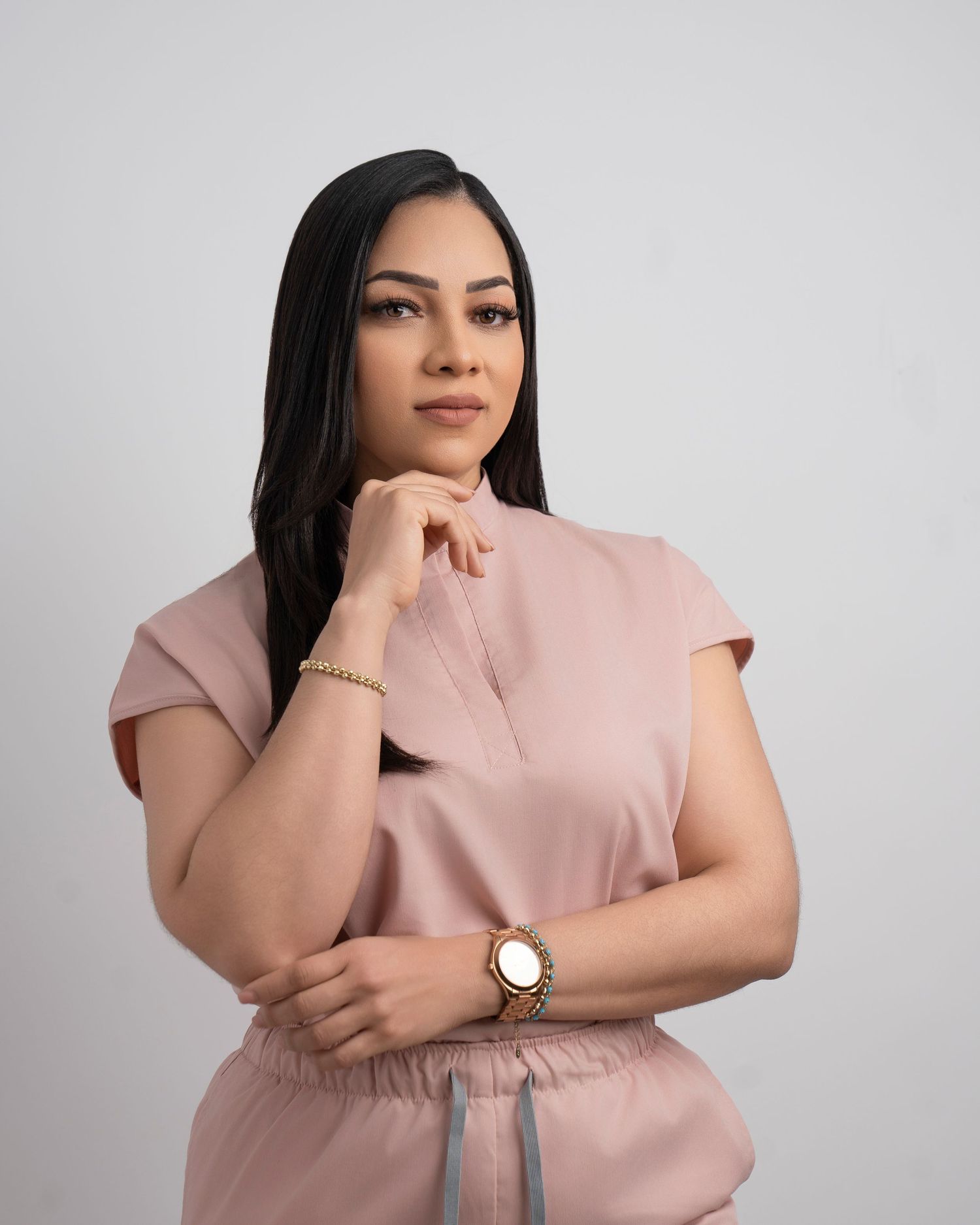 Stylish portrait in a dusty pink outfit with elegant accessories and thoughtful pose against neutral backdrop.