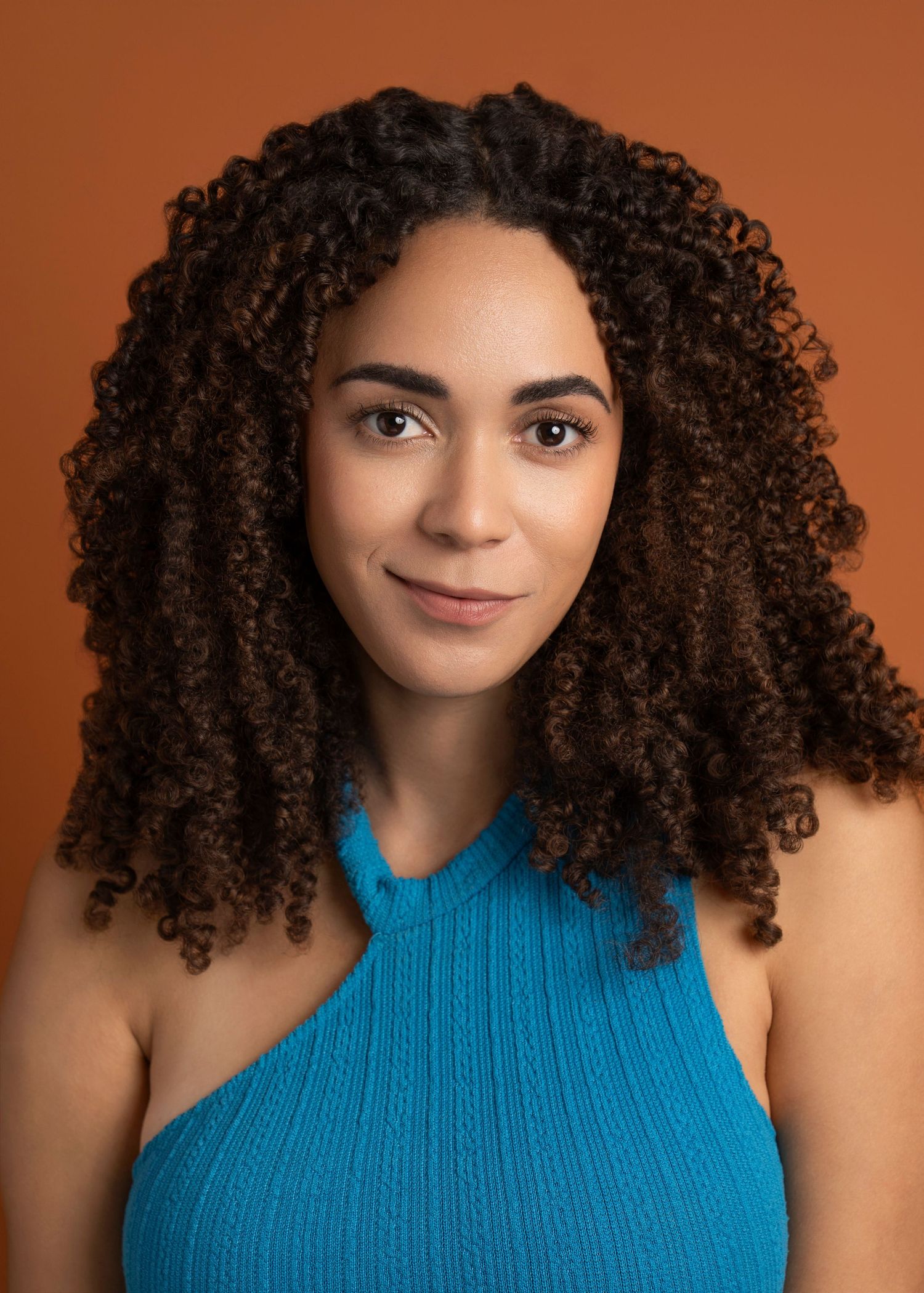 Portrait with natural curly hair and blue halter top against orange background.