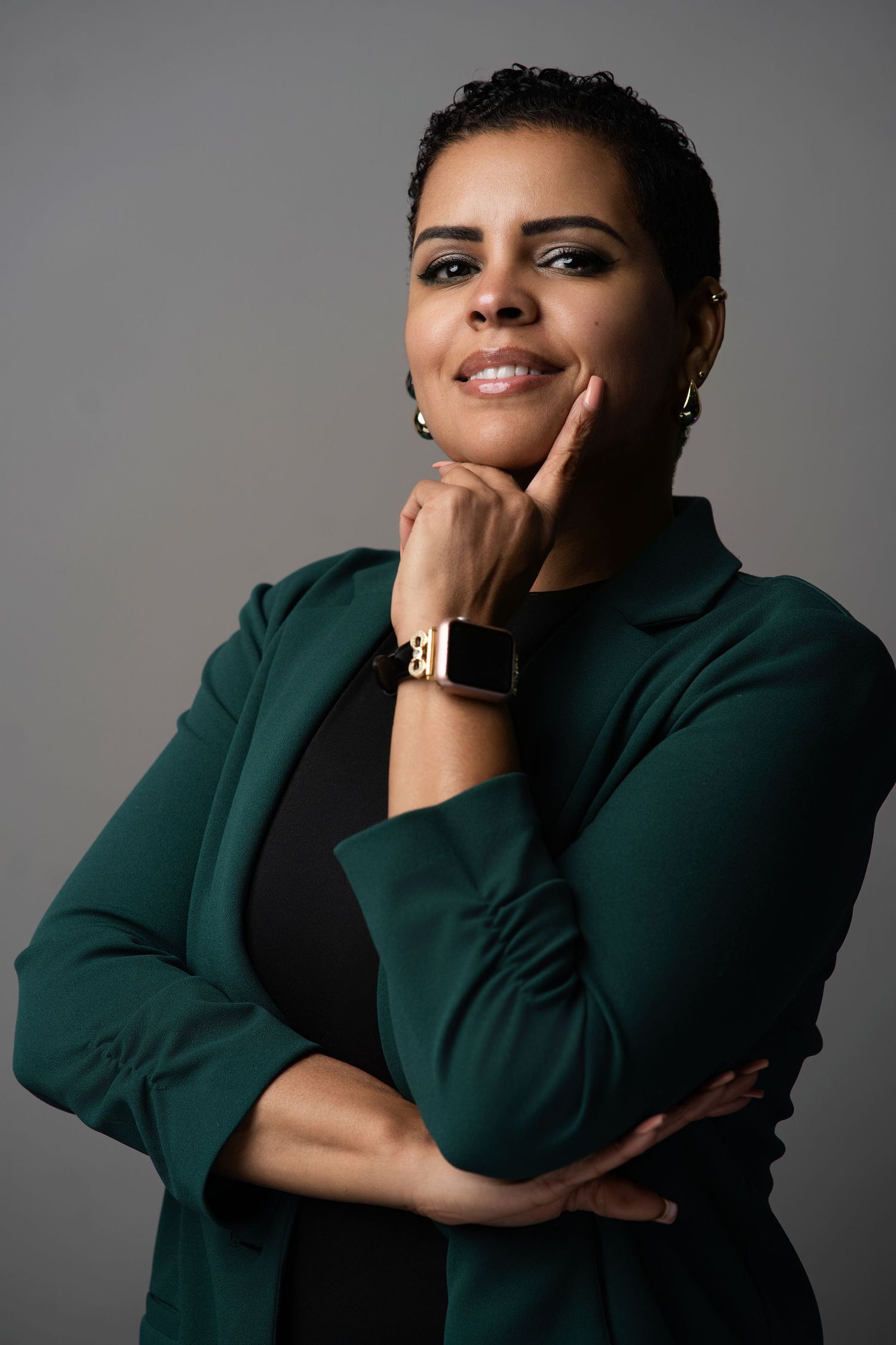 Professional portrait in dark green blazer with confident pose against gray background.