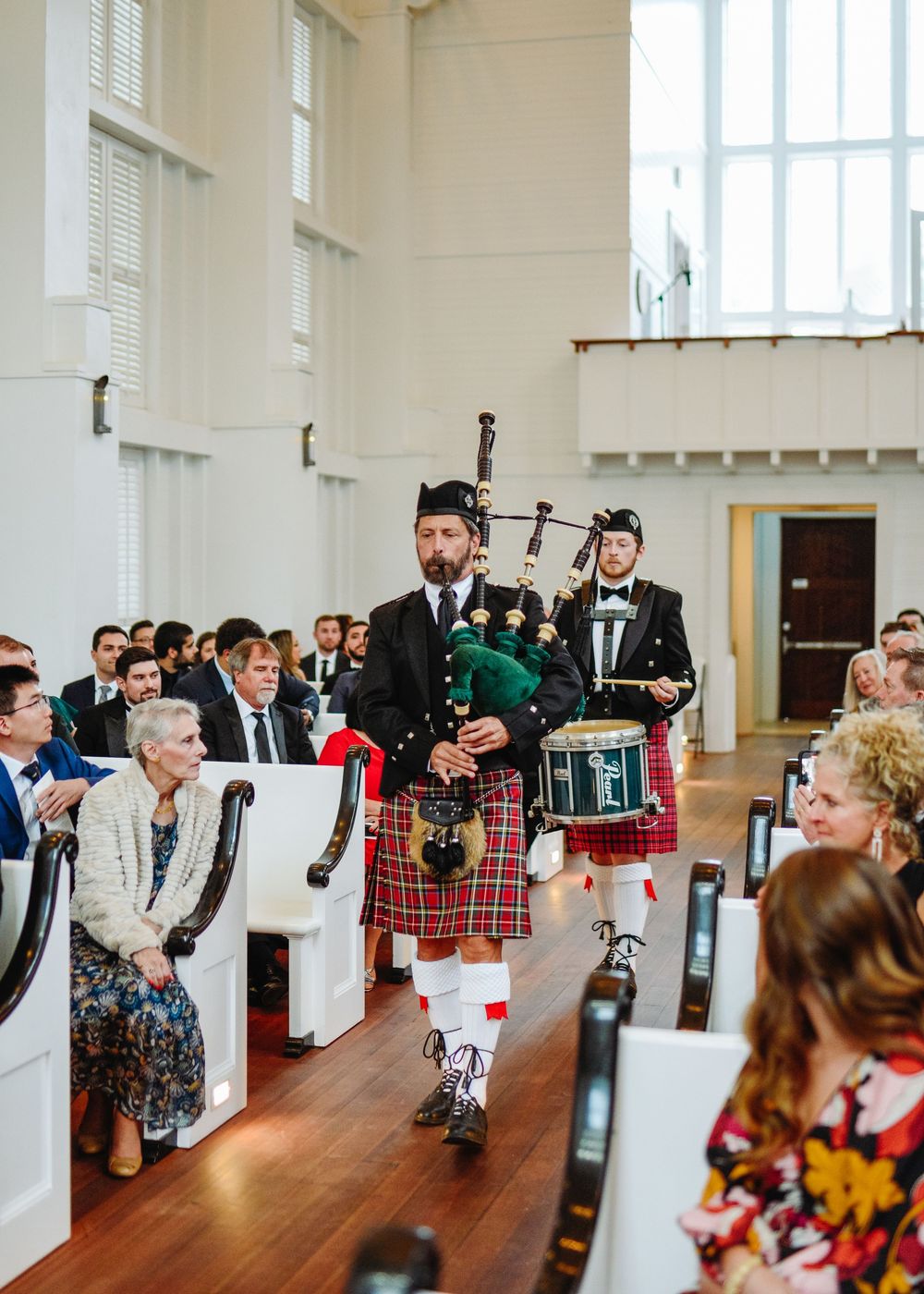 Bagpipers in traditional Scottish kilts perform during a wedding ceremony procession in a bright church sanctuary.