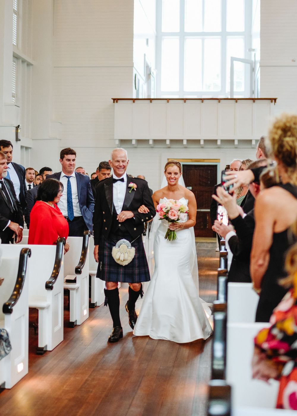 Wedding ceremony guests seated in white chairs watch as couple shares romantic dance on wooden floors.