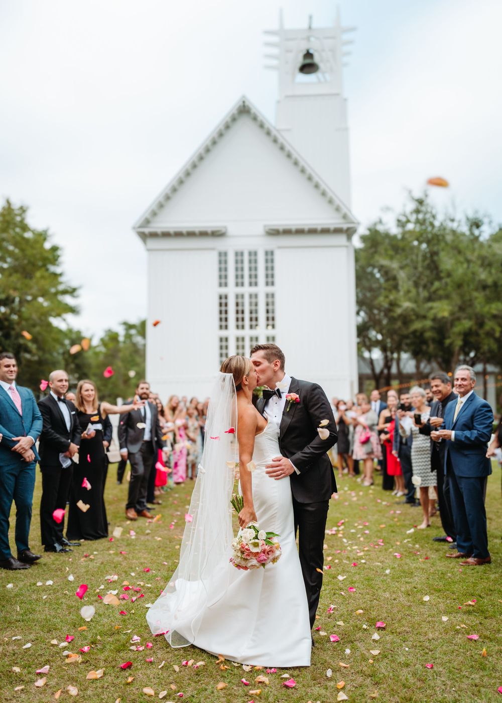 Celebratory moment outside a white chapel as guests shower confetti on the newlyweds.
