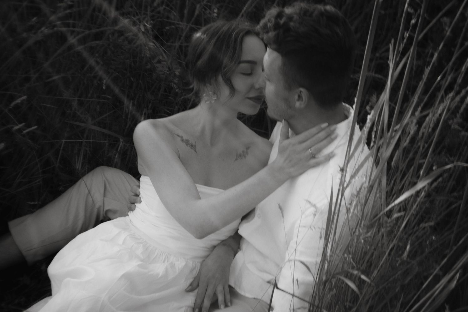 A romantic black and white photo series of a couple embracing intimately in tall grass and natural settings.