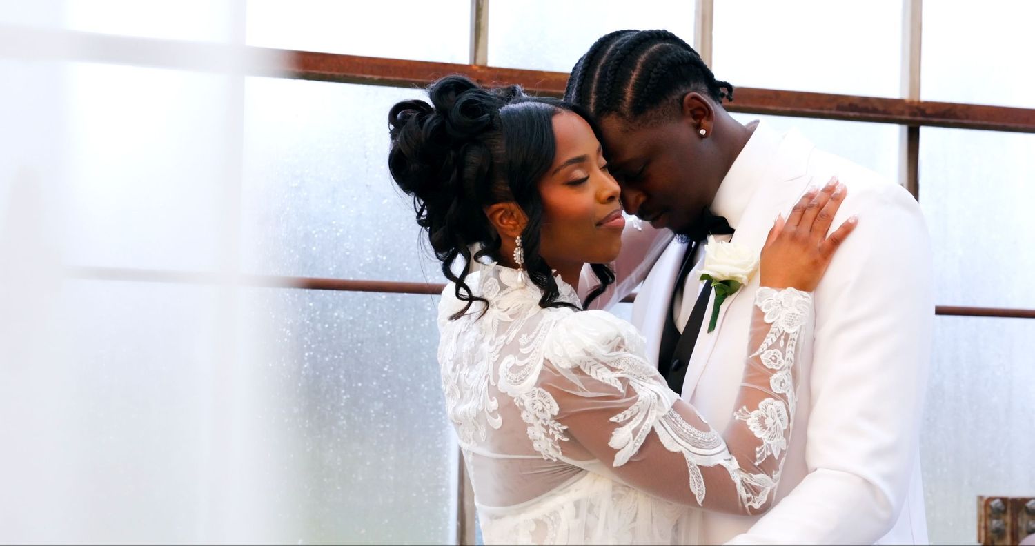 A couple shares a romantic moment in formal white attire during what appears to be a wedding celebration.