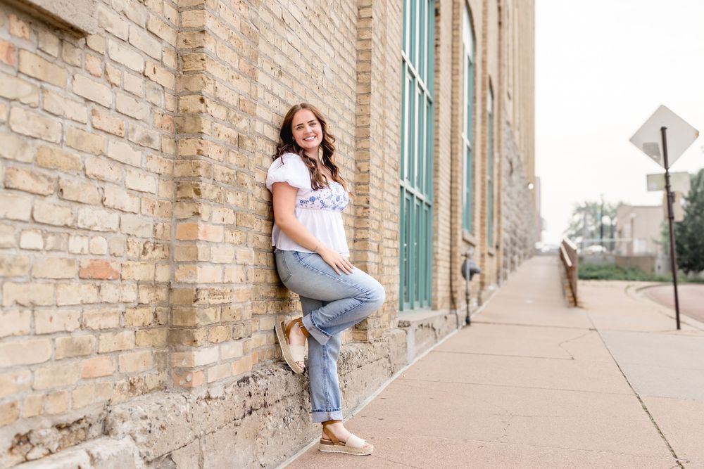 Person in casual outfit posing against textured brick wall with turquoise window frames.