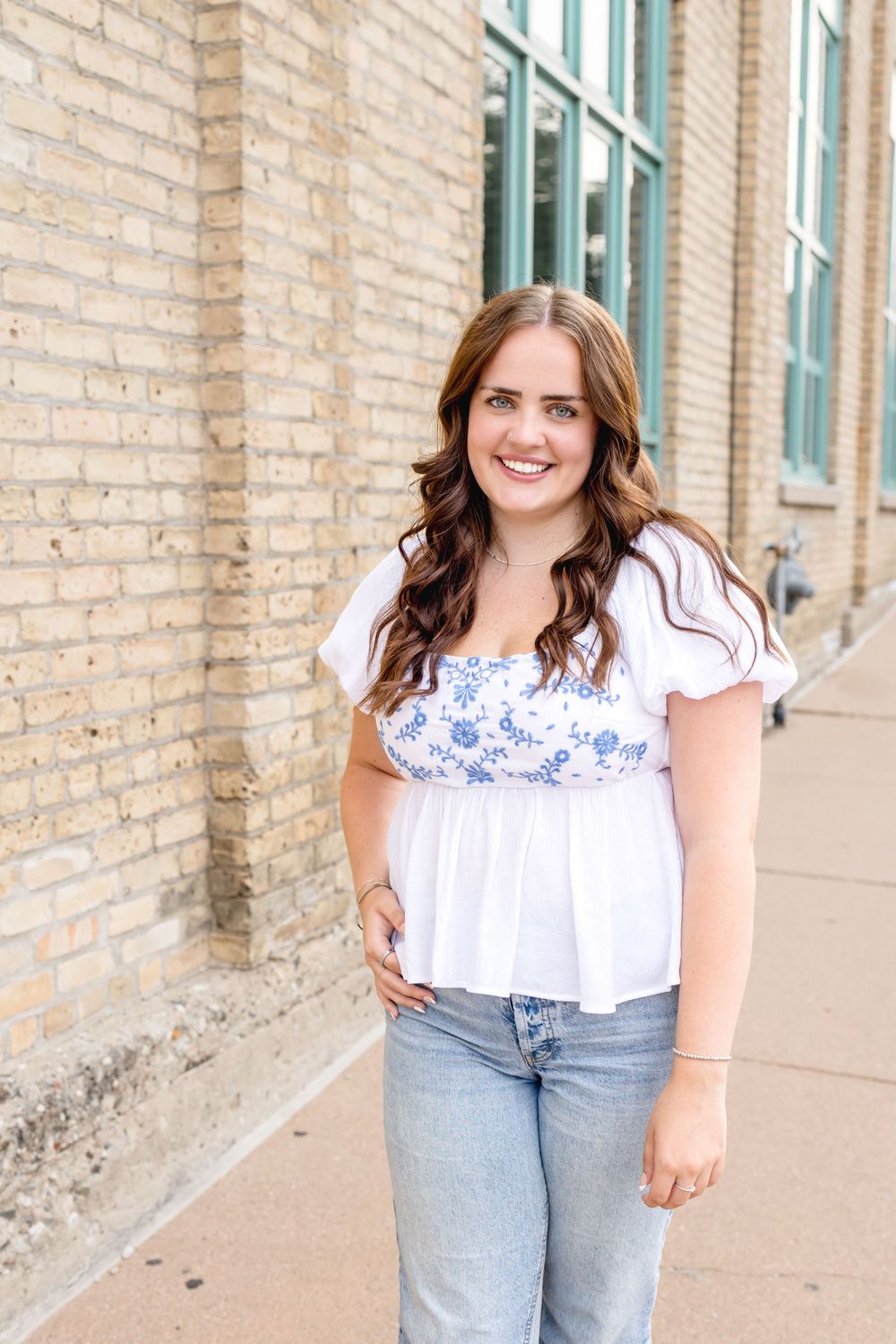 Stylish summer outfit featuring white peasant top and light denim against brick wall.