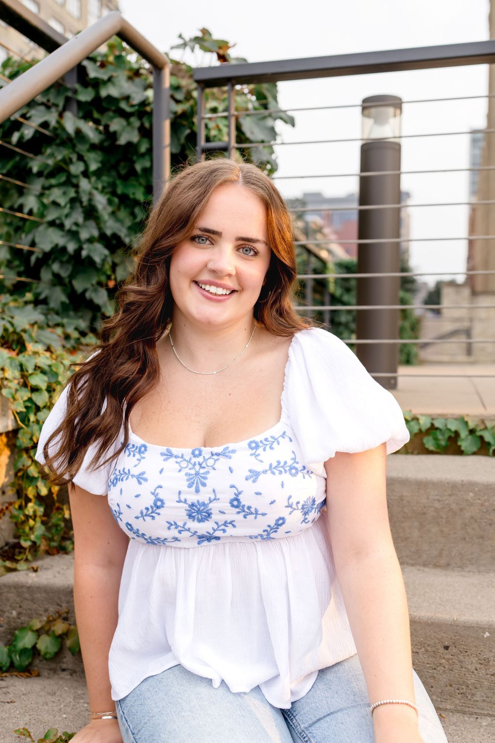 A casual portrait on outdoor steps features a white and blue floral top paired with light denim.