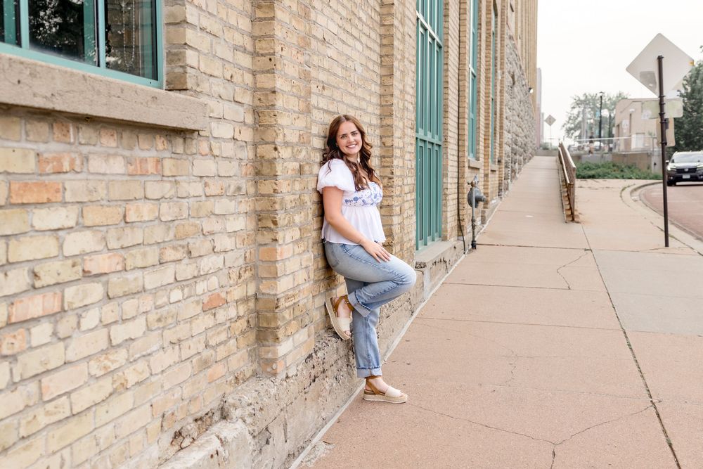 Subject leaning against beige brick building with large turquoise-framed windows.