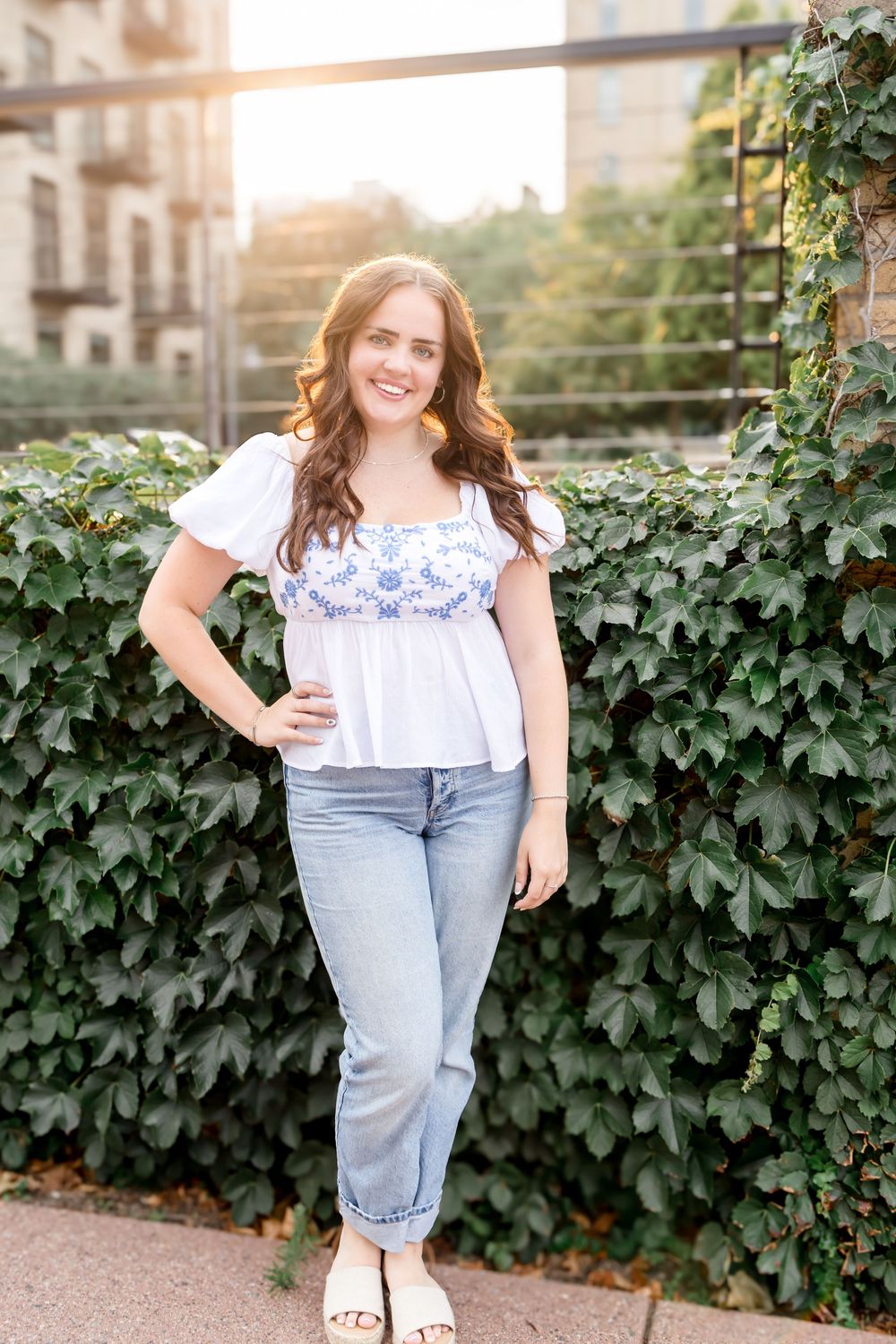 Outdoor fashion photo against climbing ivy wall featuring white peasant top and relaxed denim styling.