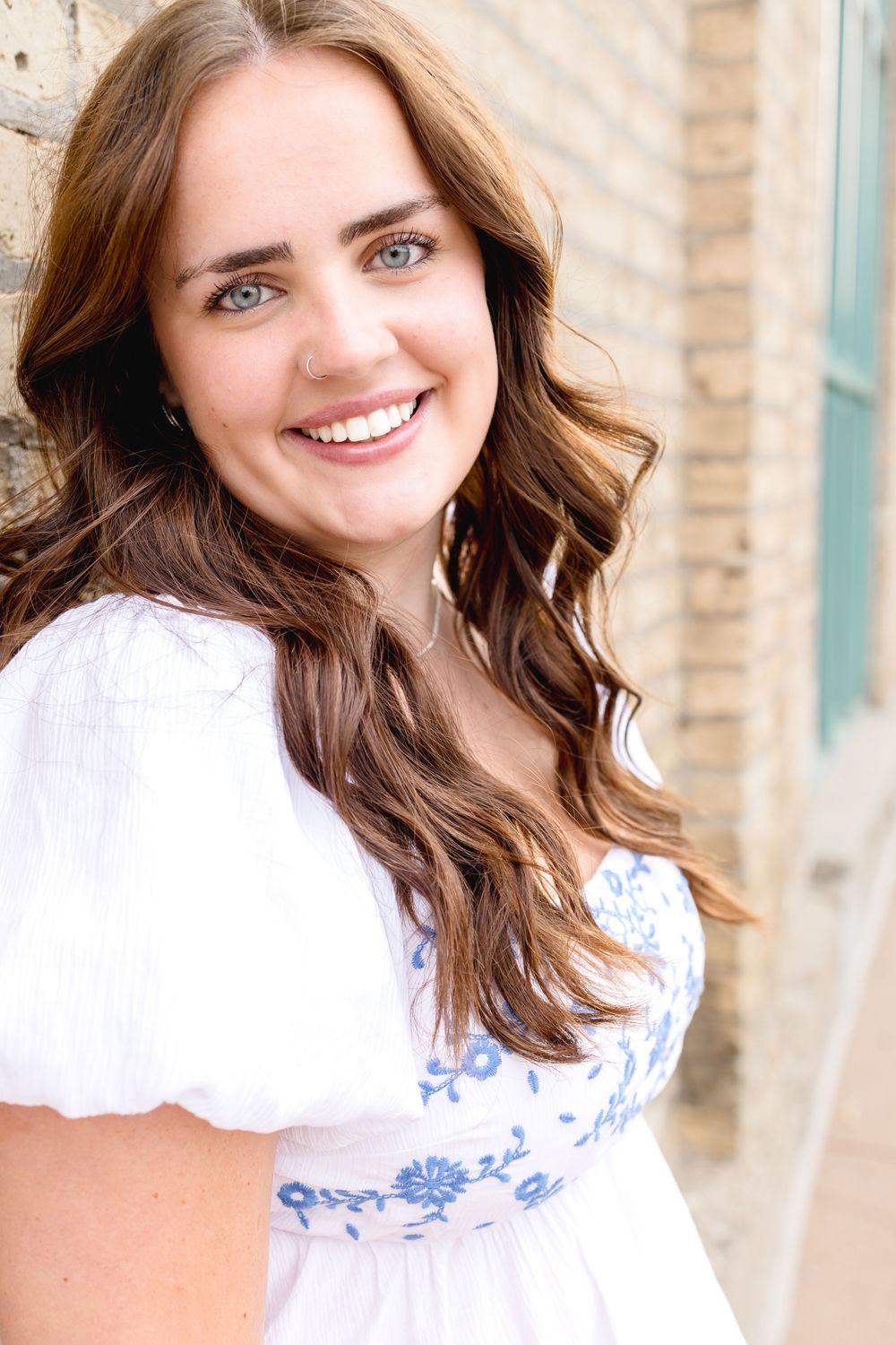 Portrait shot showing bright smile and white peasant top with blue embroidery details.