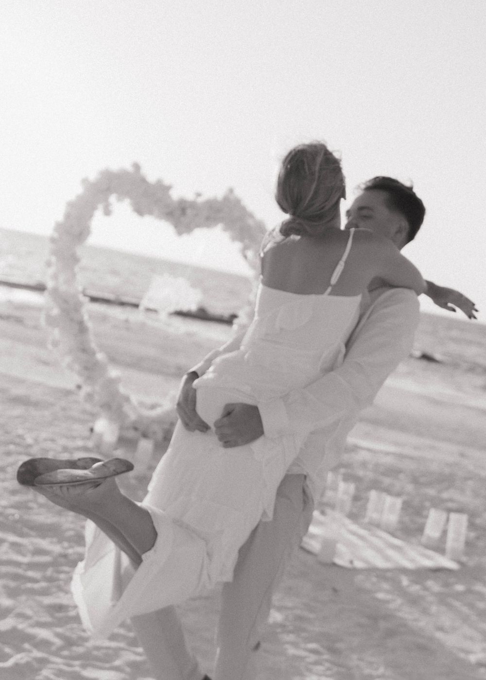 Romantic proposal portrait under a white heart arch on Honeymoon Island, Florida at sunset.