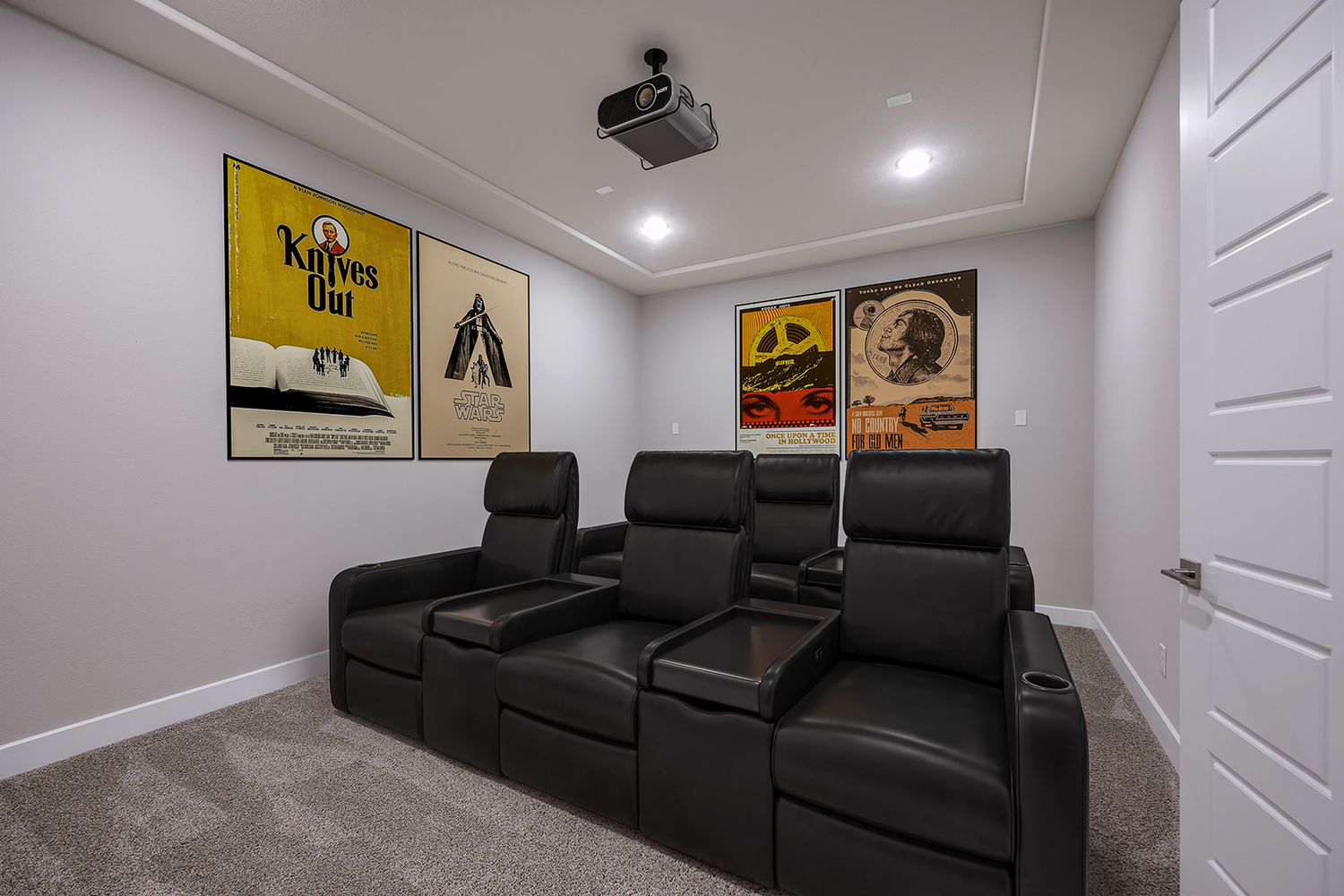 Home theater room with black leather recliners and yellow movie posters mounted on gray walls.