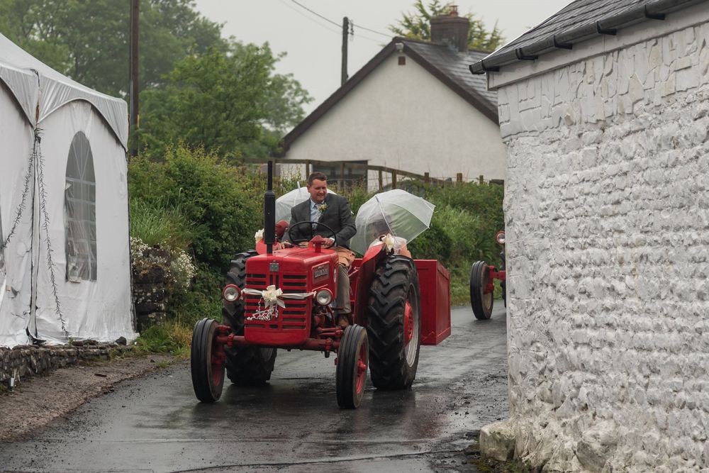 A vintage red tractor parked outside a traditional white-walled building in the countryside.