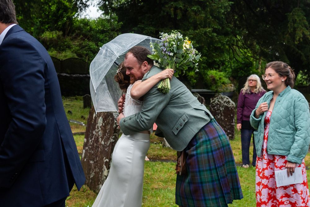 Wedding guests gathered outdoors wearing a mix of formal attire and traditional Scottish kilts.