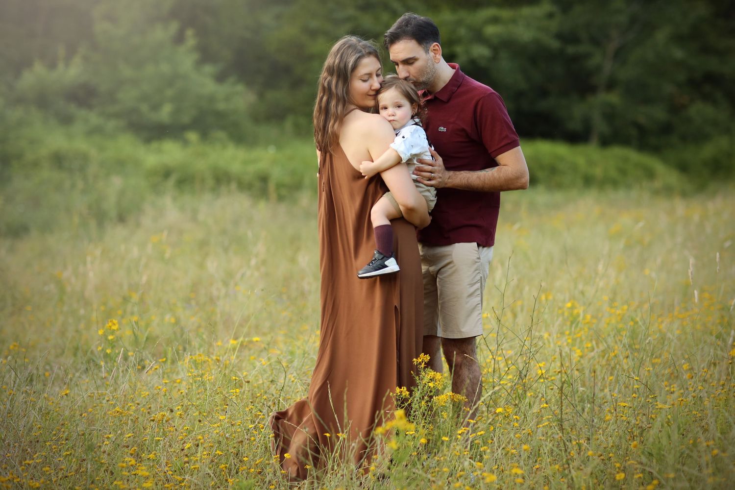 A couple holds their baby while standing in a wildflower meadow on a summer afternoon.