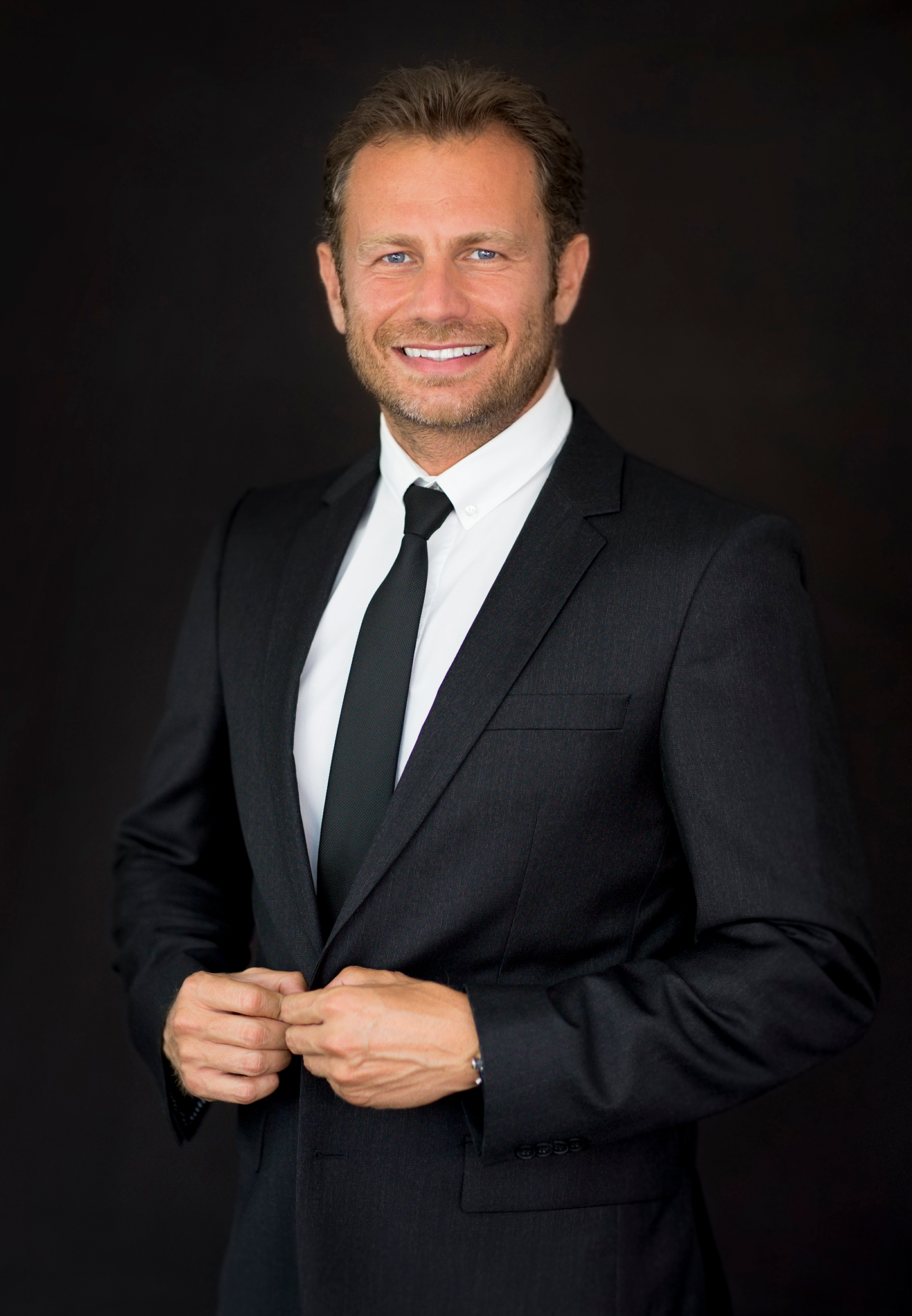 Professional portrait sequence showing a person in a black suit and tie adjusting their jacket against a dark background.