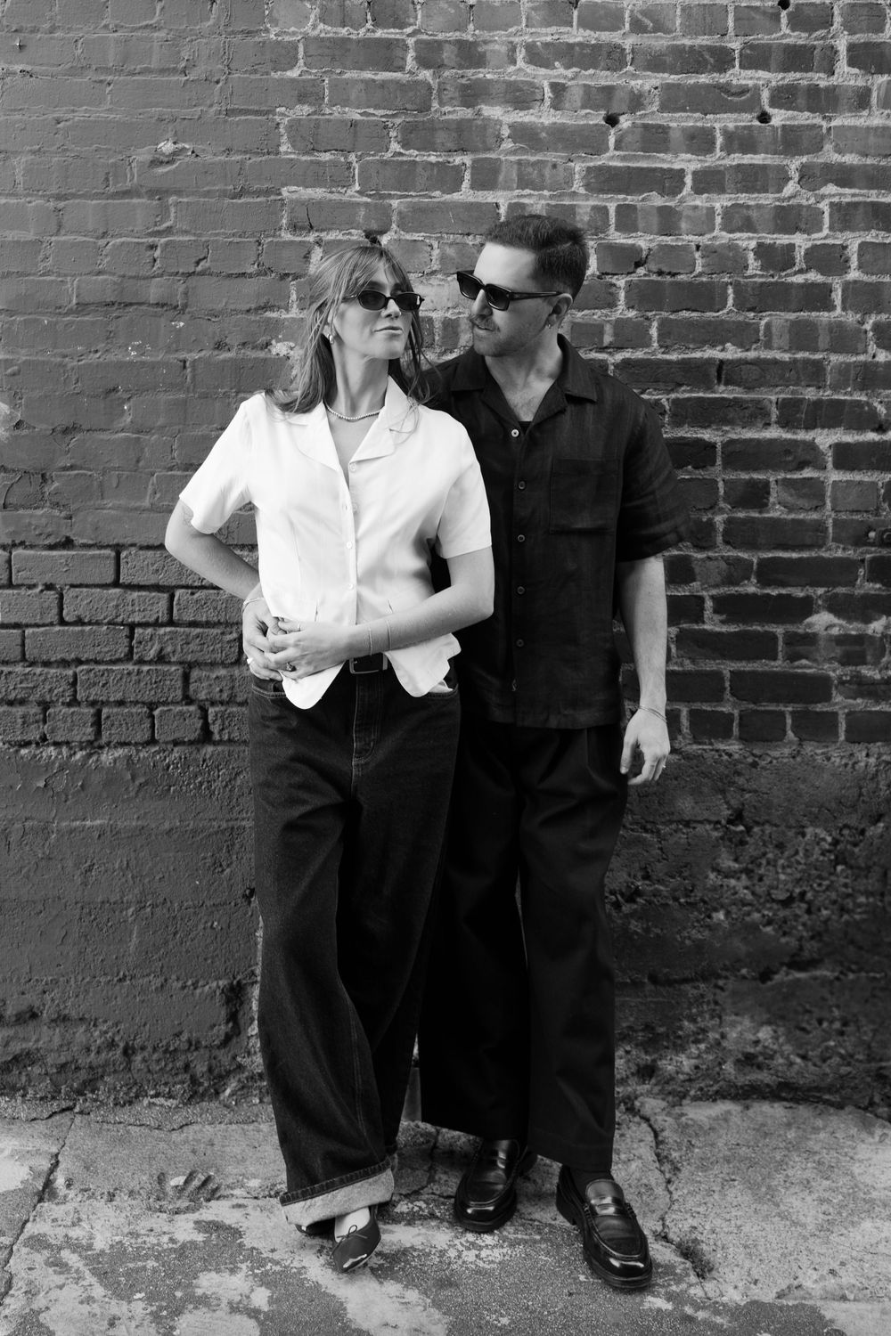 A couple poses casually against a brick wall in contrasting black and white outfits.
