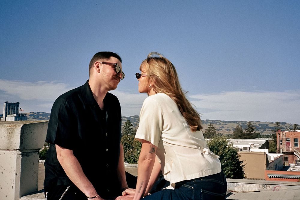 Couple in coordinated outfits sitting on a rooftop with mountains visible in the background.