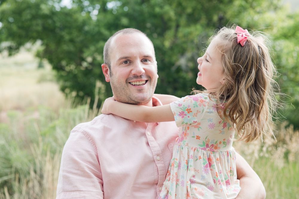 A parent and child share a joyful moment together outdoors in a field with soft natural lighting.