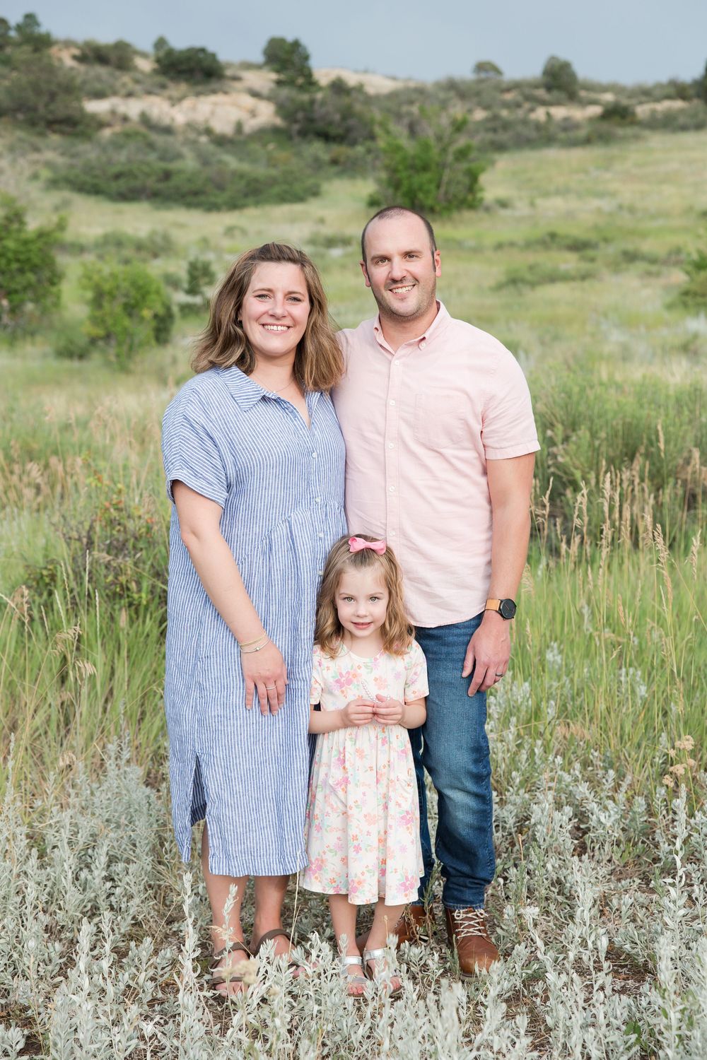 A family poses together in a field of sage brush and wildflowers against a rolling hillside landscape.