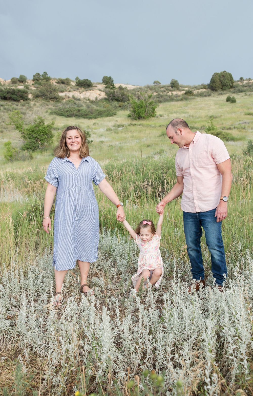 Family enjoying a sunny day together in a wildflower meadow with rolling hills in the background.