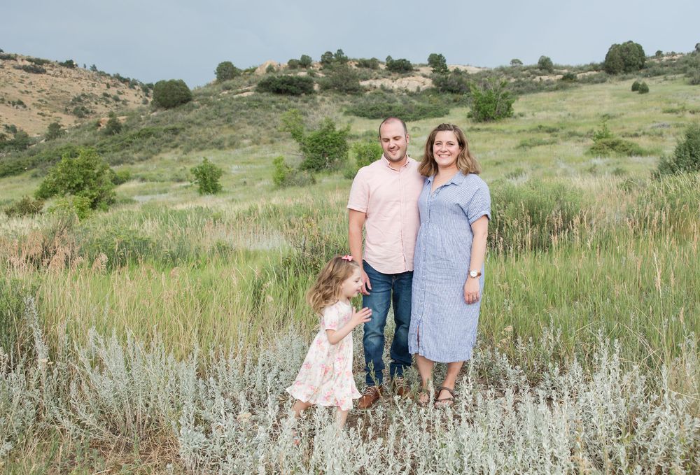 Family in coordinated outfits having their portrait session taken in a scenic mountain meadow landscape at sunset.
