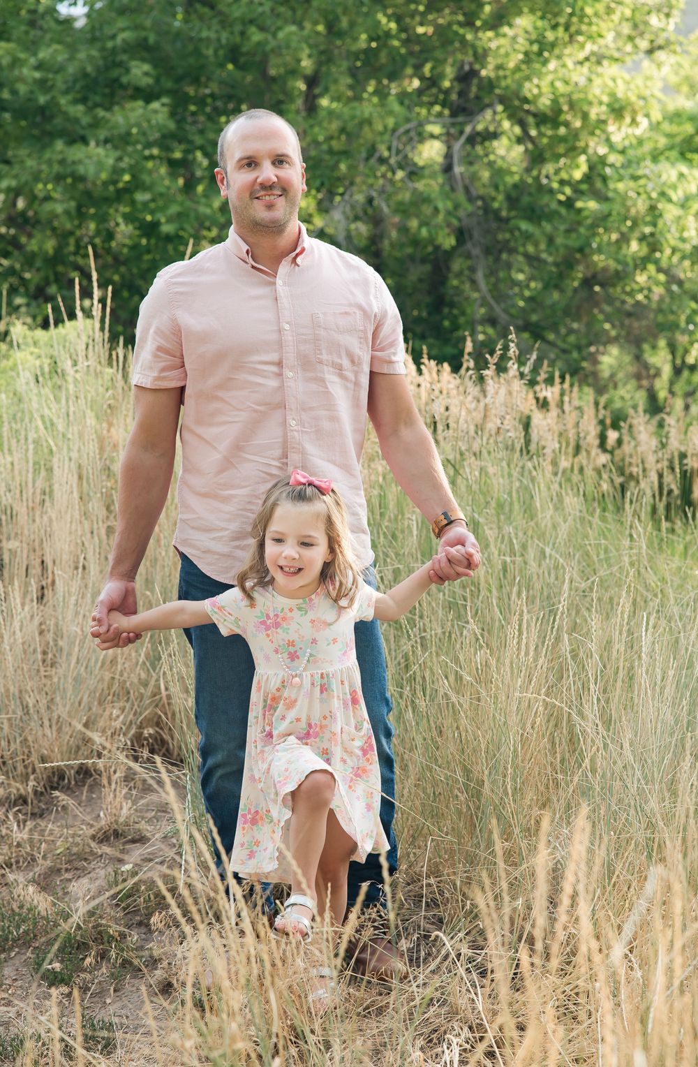 Parent and young child walking together and holding hands among tall golden grass in an outdoor nature setting.