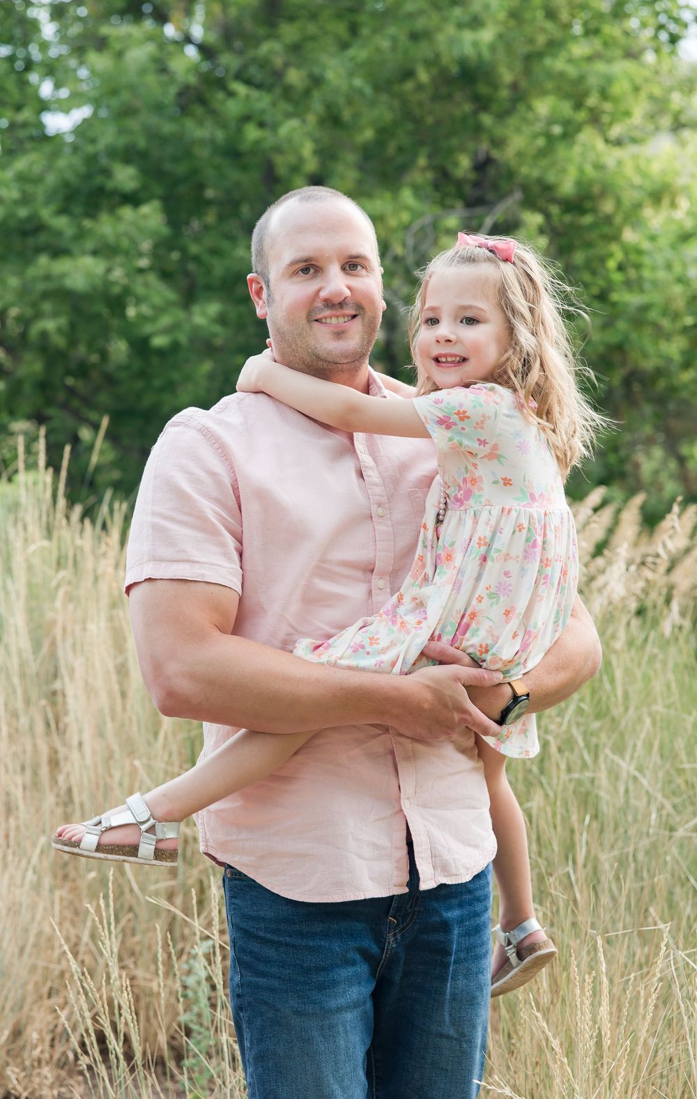 A parent and child share a tender moment while posing together in a field of tall grass on a sunny day.