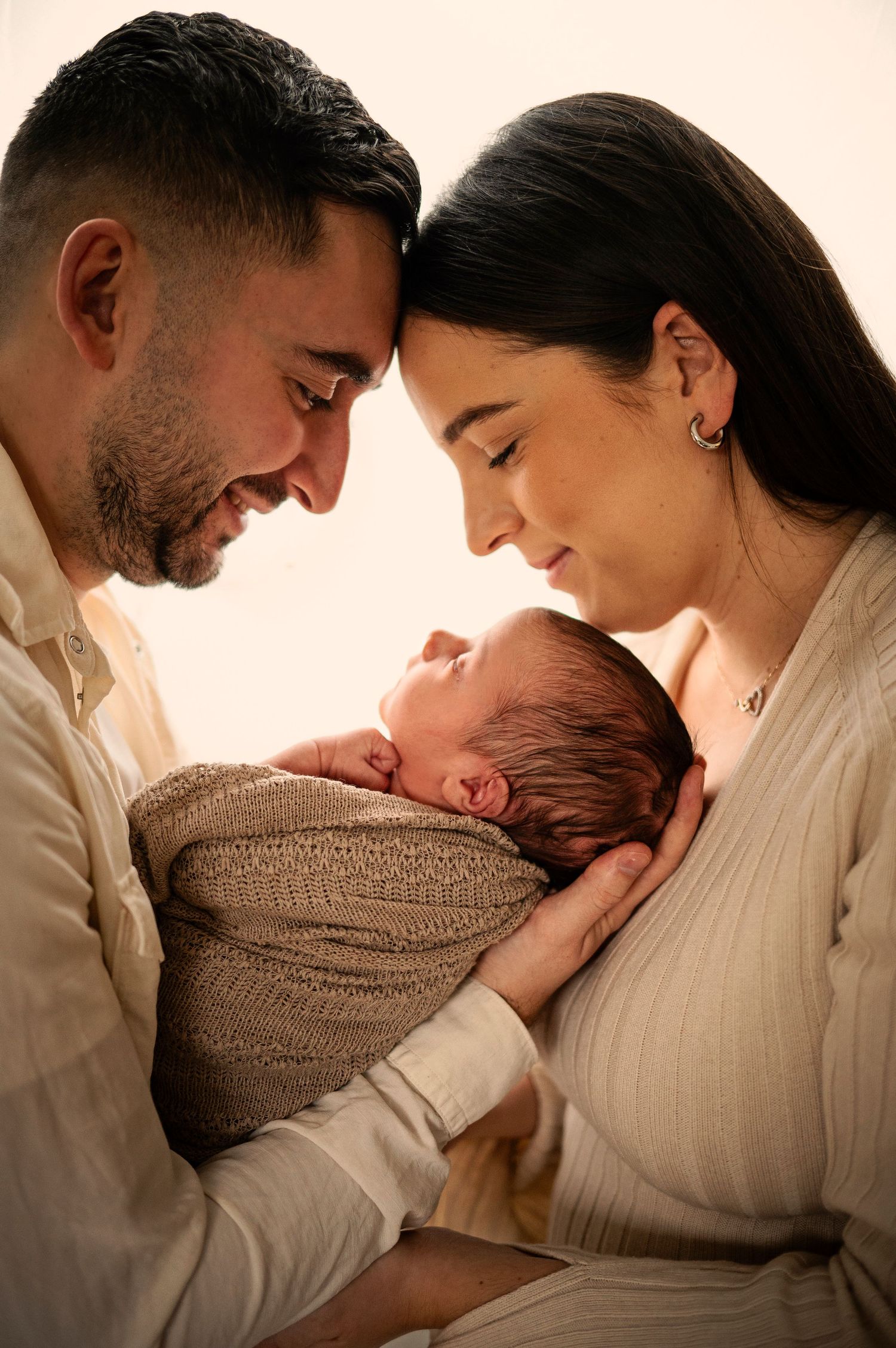 A tender family moment as parents gaze lovingly at their newborn baby wrapped in a brown swaddle.