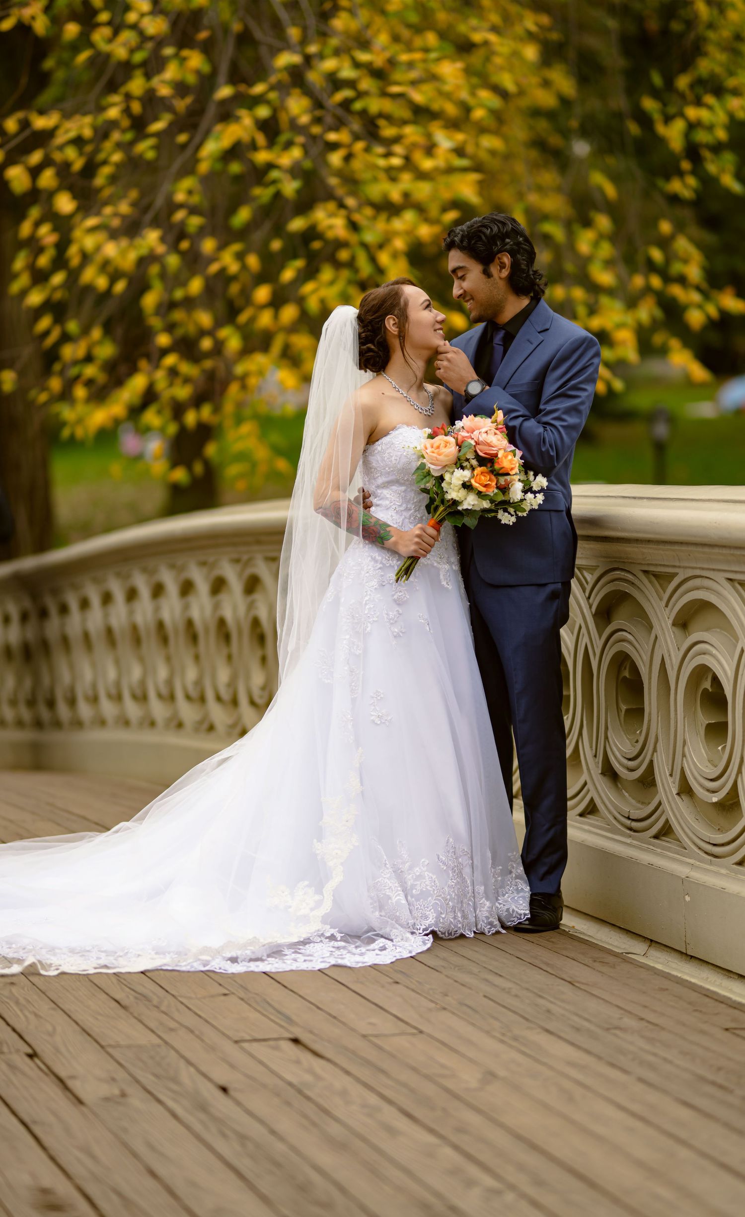Romantic autumn wedding portrait on a bridge with yellow foliage in the background.