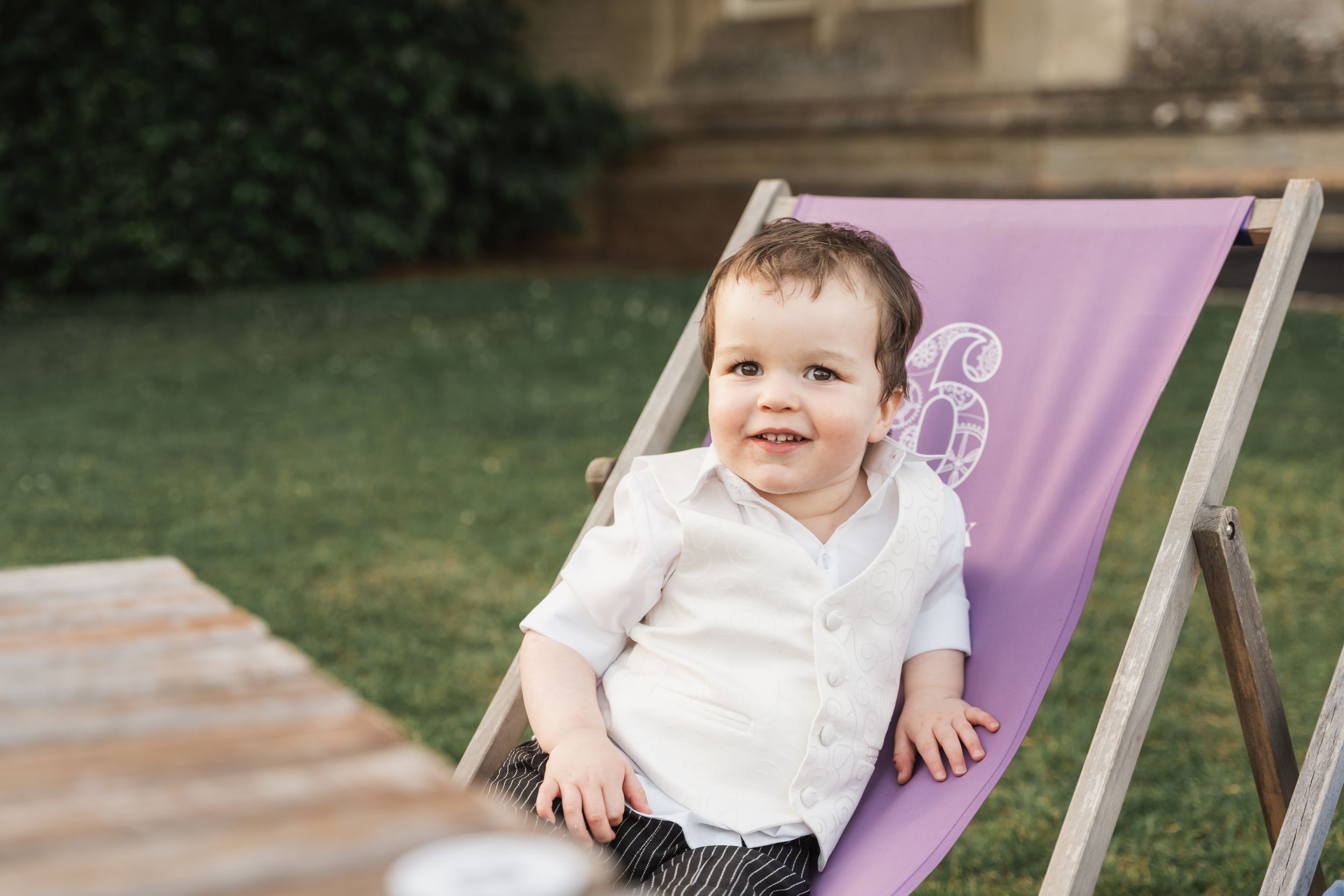 A child wearing a white shirt sits in a purple lawn chair on a wooden deck.
