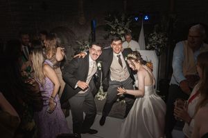 Wedding guests dance and celebrate together at a dimly lit reception venue with blue accent lighting in the background.