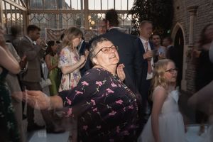 A guest in a dark floral print dress dances enthusiastically at an indoor wedding reception.