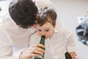 Two people sharing a sip from a green glass bottle while wearing white shirts.