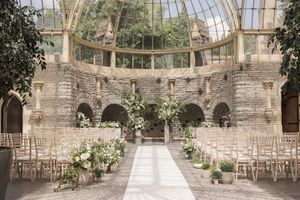 Elegant greenhouse wedding venue with stone walls and rows of white chairs set up for a ceremony.
