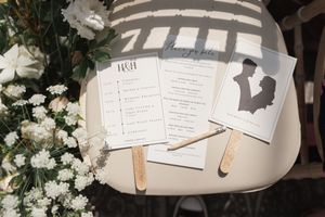 Wedding program fans and event details displayed with white flowers on a light colored surface.
