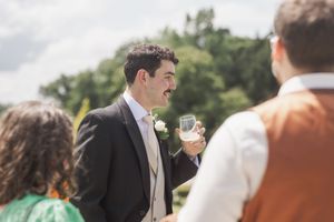 Well-dressed wedding guest enjoys conversation and drinks at outdoor reception.