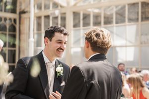Two people share a lighthearted moment during a sunny outdoor wedding conversation.